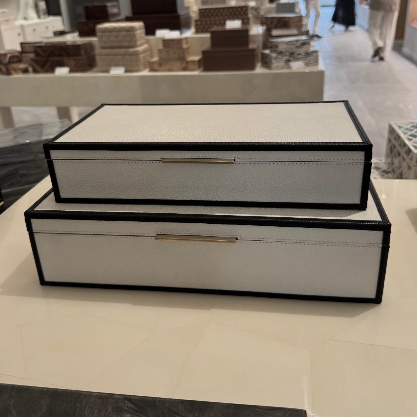 Two black and white jewelry boxes on a table with a store interior in the background.