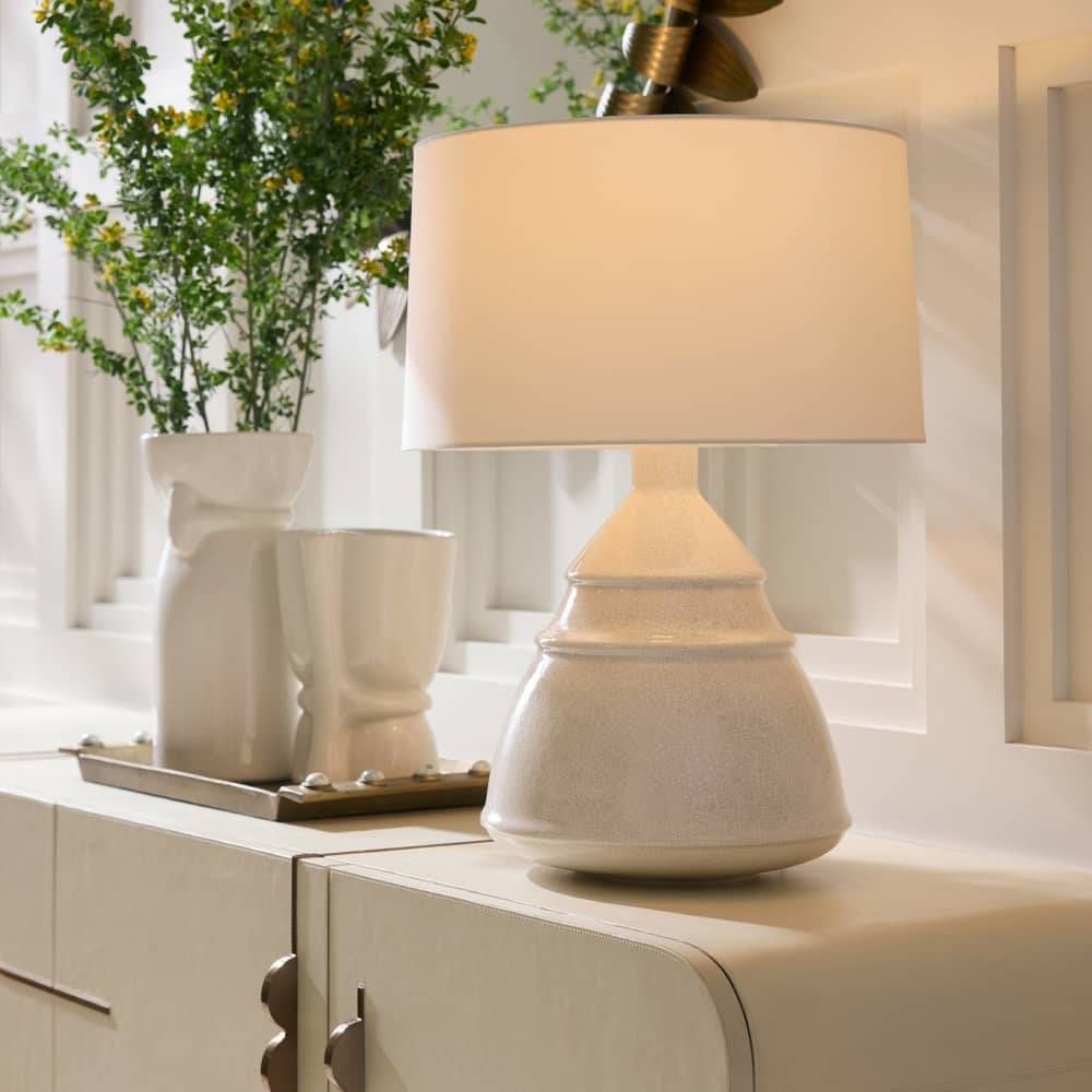 White ceramic table lamp on a surface with decorative items in the background