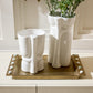 Two white ceramic vases on a decorative tray with a plant in the background.