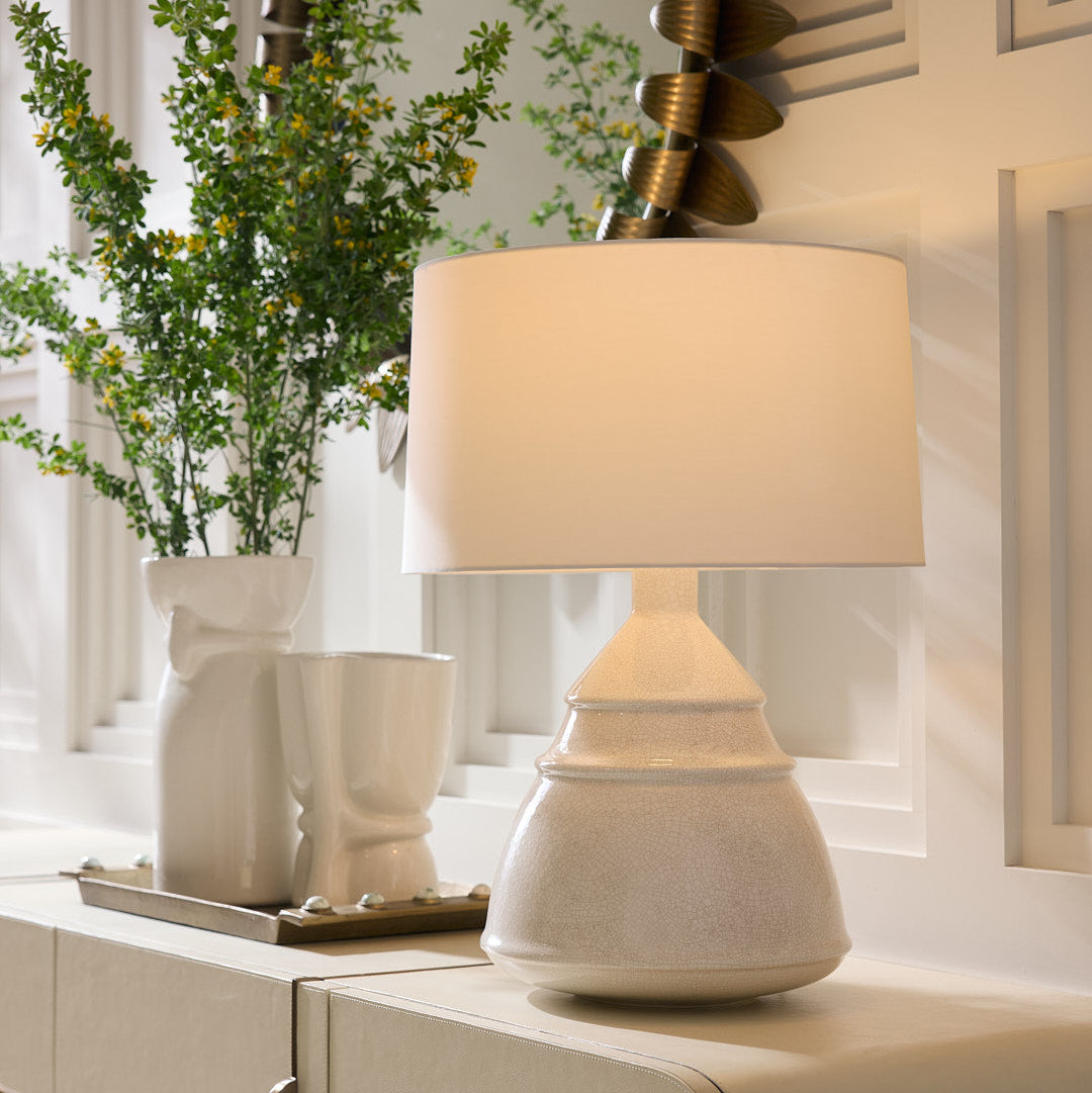 White ceramic lamp on a cabinet with decorative plants in the background