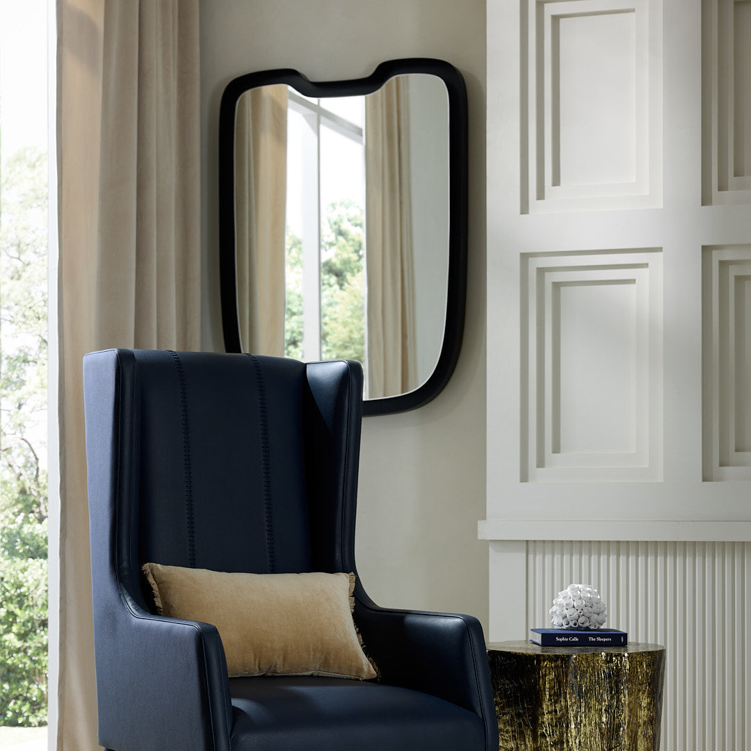Black leather armchair with a gold side table in a room with a mirror and decorative elements.