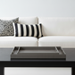 A modern white fabric sofa in a minimalist living room setting, with a glass-top coffee table in front holding a dark gray rectangular tray.