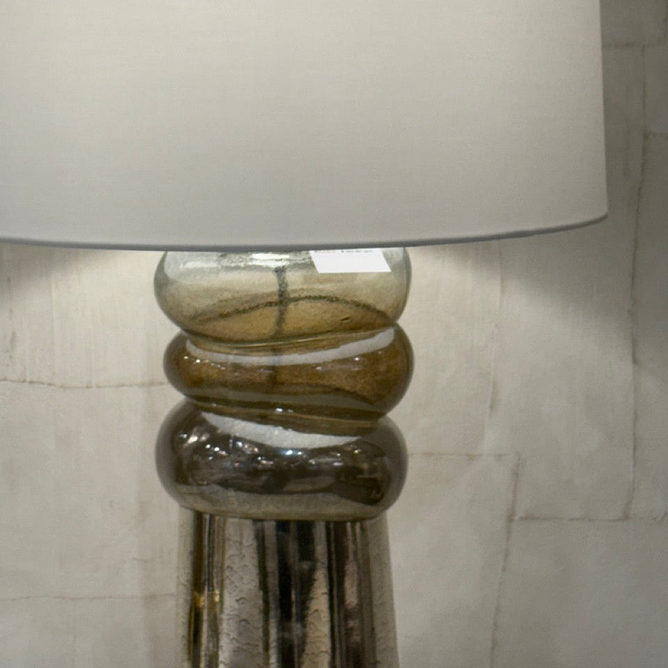 Table lamp with a clear glass base and white shade on a neutral background