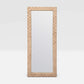 A tall, narrow rectangular floor mirror with a woven natural fiber frame in a light tan color, shown against a neutral light gray background.