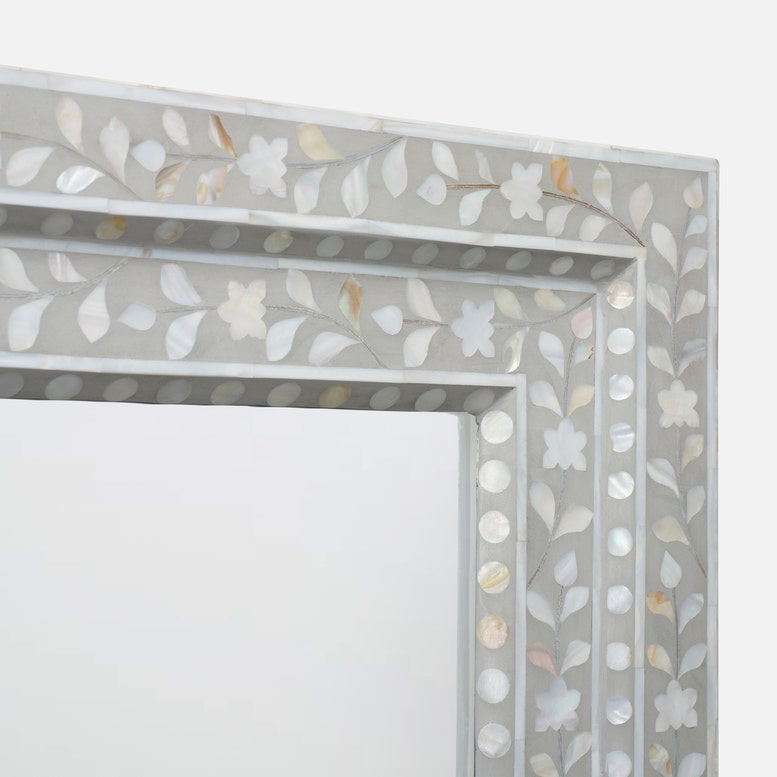A close-up of a decorative rectangular mirror frame featuring a mother-of-pearl inlay of white and pale gold floral and leaf motifs on a light gray background.