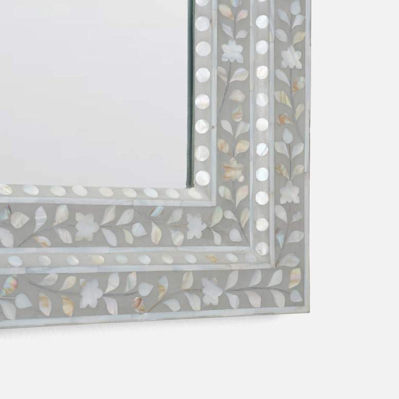 Close-up of a decorative rectangular mirror frame with a silver-gray border and inlay of white, iridescent mother-of-pearl floral and leaf motifs.