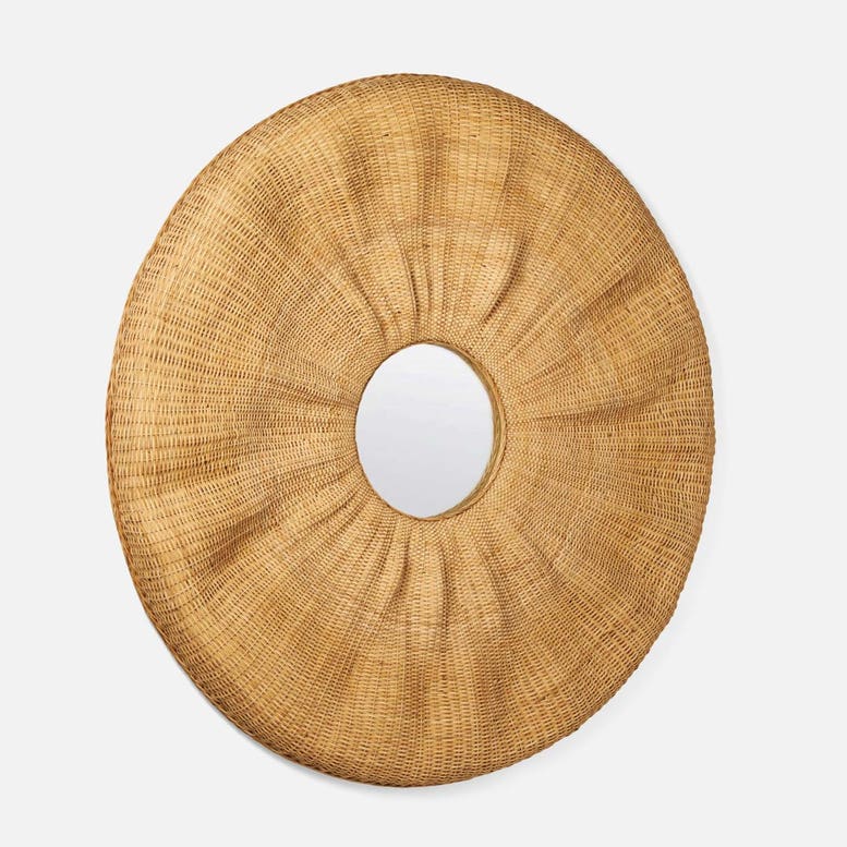 A round woven rattan wall mirror with a sunburst design and a central oval mirror, shown against a light gray background.