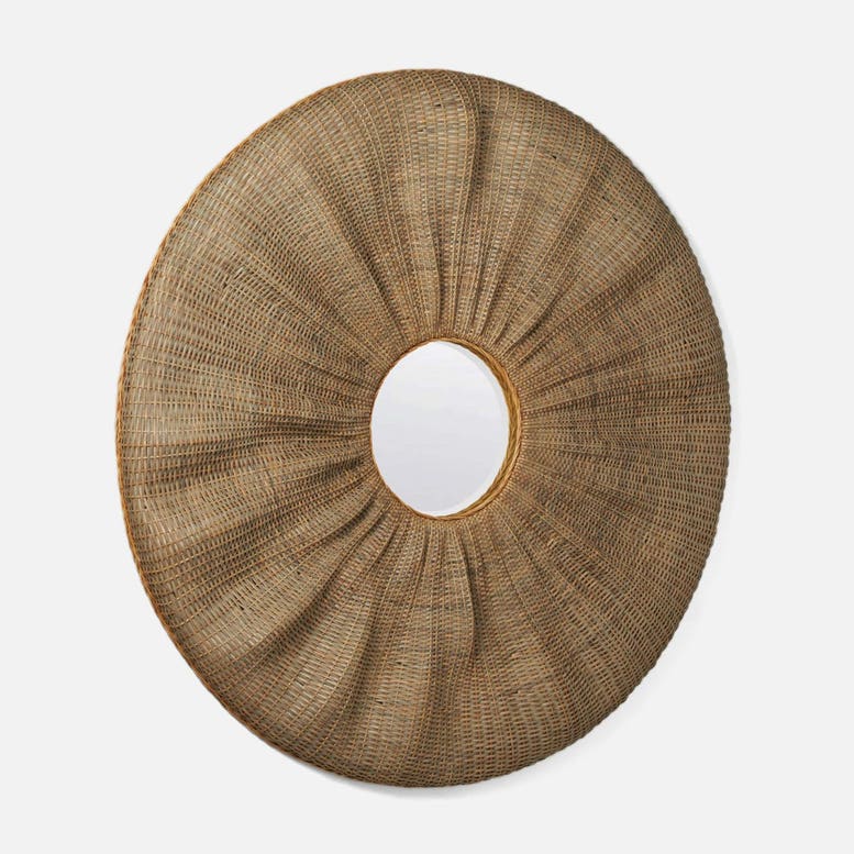 A round woven rattan wall mirror with a sunburst design and a central oval mirror cutout, shown against a light gray background.