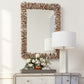 Decorative mirror with natural frame, lamp, and flowers on a white wall.