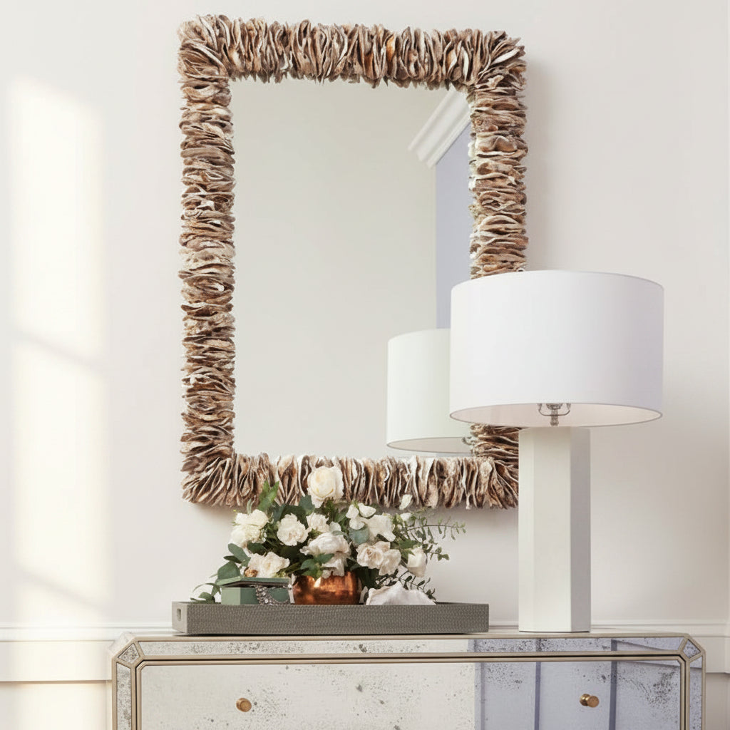 Decorative mirror with natural frame, lamp, and flowers on a white wall.