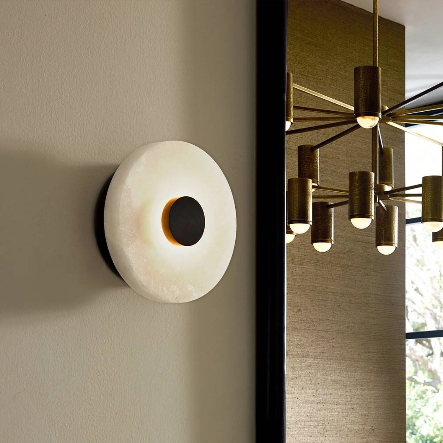 Modern wall sconce on a neutral wall with a chandelier in the background
