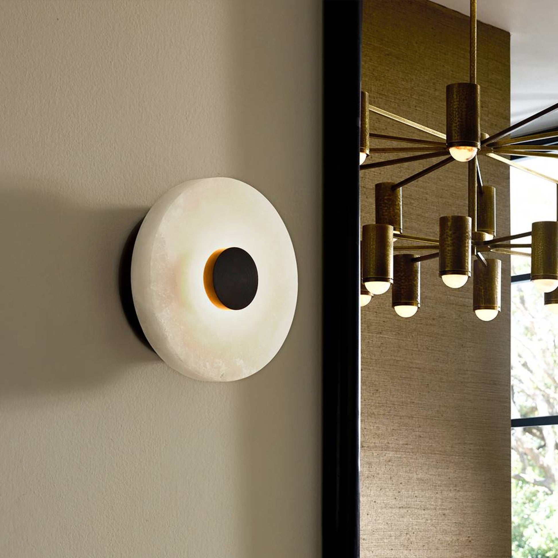 Modern wall sconce on a neutral wall with a chandelier in the background