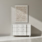 White dresser against a gray wall with a textured wall art piece above it.