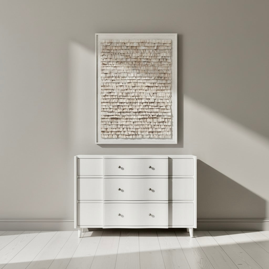White dresser against a gray wall with a textured wall art piece above it.