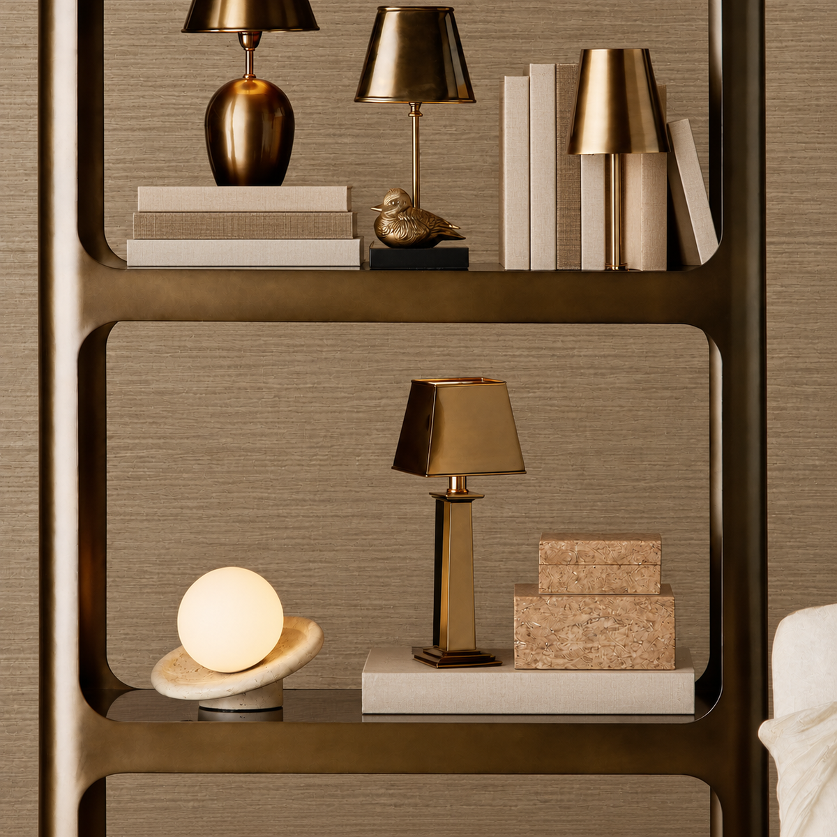 A styled interior shelf scene with multiple table lamps, books, and decor objects against a textured wall. The most prominent sellable item appears to be the tall rectangular brass table lamp centered on the middle shelf, shown alongside other home decor pieces.