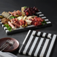 Charcuterie board with meats, cheeses, and fruits on a black and white striped platter.
