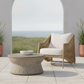 Wicker chair with white cushions and matching table on a patio with a scenic view.