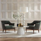 Modern living room with two dark green chairs, a white round table, and decorative items against a paneled wall.