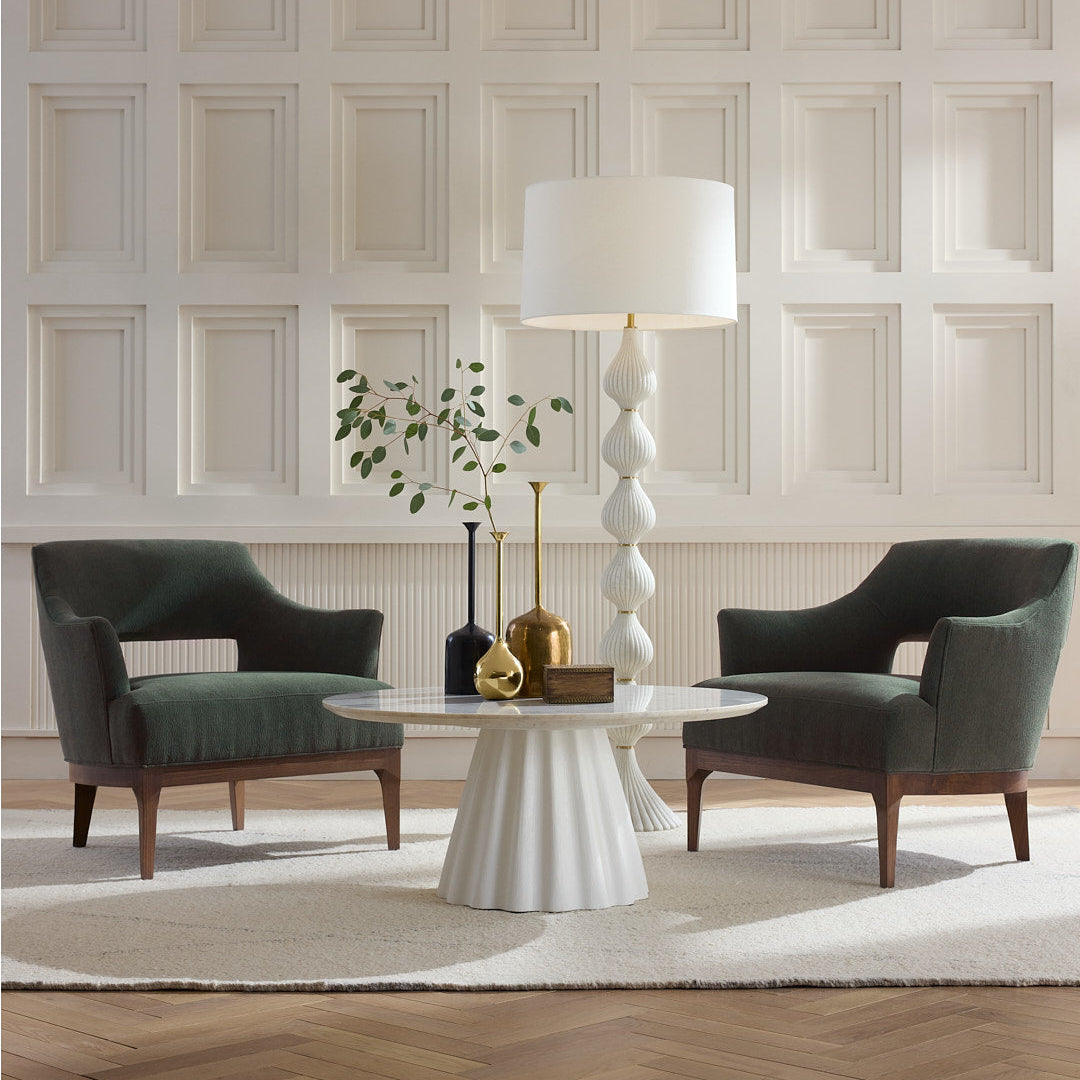Modern living room with two dark green chairs, a white round table, and decorative items against a paneled wall.