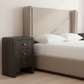 Beige upholstered bed with white pillows and a dark wooden nightstand in a room. octavia bed