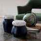 Two black stools with stone tops on a marble surface, with a green armchair and globe in the background.