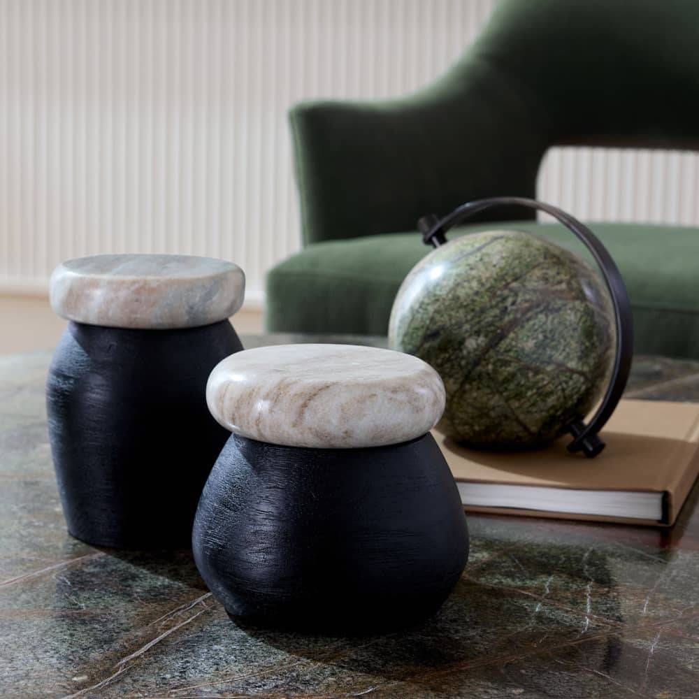 Two black stools with stone tops on a marble surface, with a green armchair and globe in the background.
