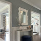 Decorative console table with mirror and blue ottoman in a room with gray walls and wooden flooring.