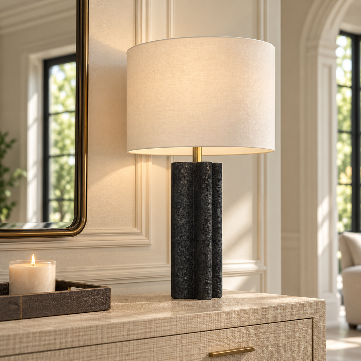 Norwood Table Lamp with a textured black sculptural base, brass accent, and ivory drum shade styled on a grasscloth console in a bright, elegant interior.