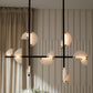 Modern chandelier with glass shades in a room with a curtain and floral arrangement.