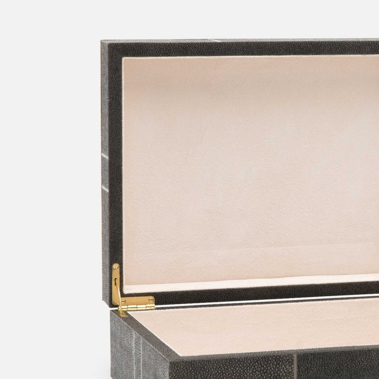 Close-up of an open luxury jewelry box with a textured black exterior, a cream-colored interior lining, and a gold hinge.