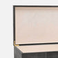 Close-up of an open luxury storage box or jewelry case with a black shagreen exterior, cream interior lining, and gold-tone hinge hardware, set against a plain light gray background.