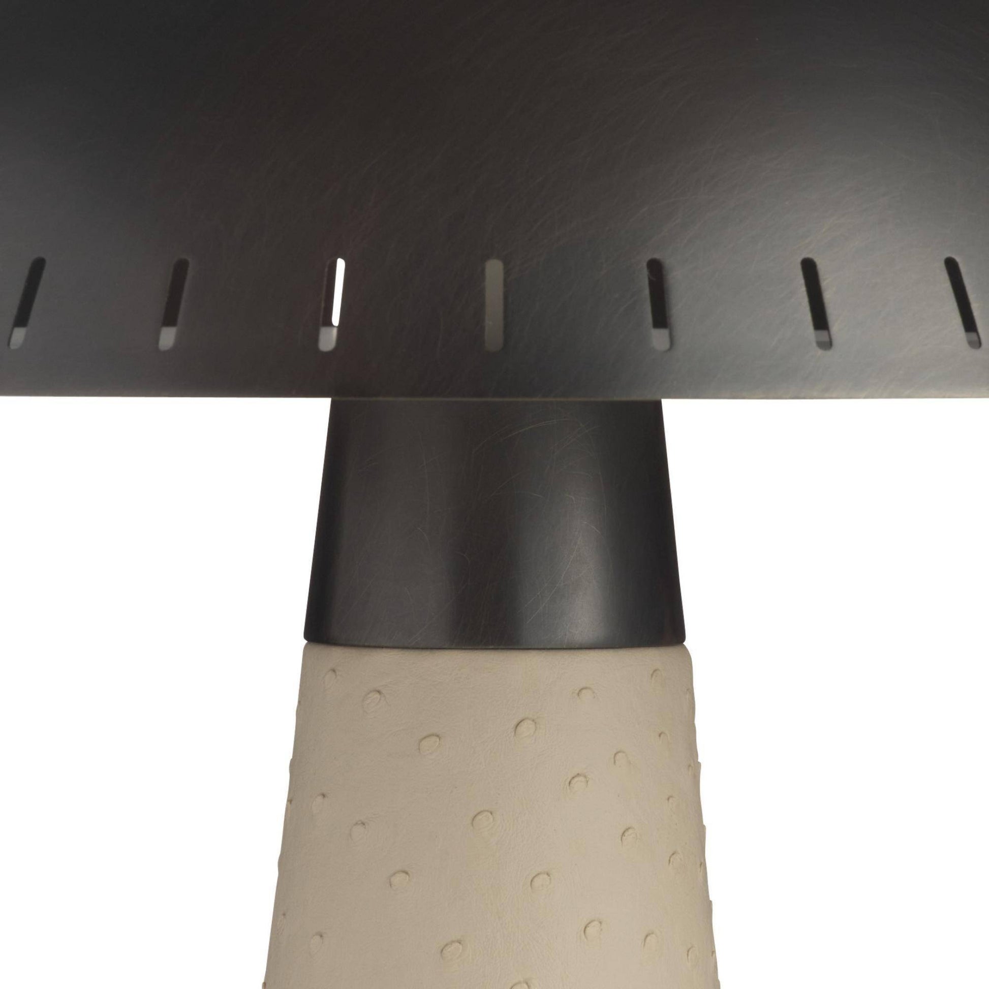 Close-up of a dark metal table or chair leg with a perforated top surface and a textured beige cylindrical base on a white background.
