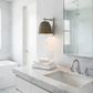 A modern bathroom vanity with a white marble countertop and sink, chrome faucet, folded white towels, a woven pendant wall sconce, and a large mirror reflecting a glass shower door.