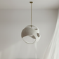 Modern pendant light hanging in a minimalistic room with white walls and curtains.