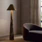 Floor lamp with a textured base and gold shade next to a gray sofa in a room with a window.