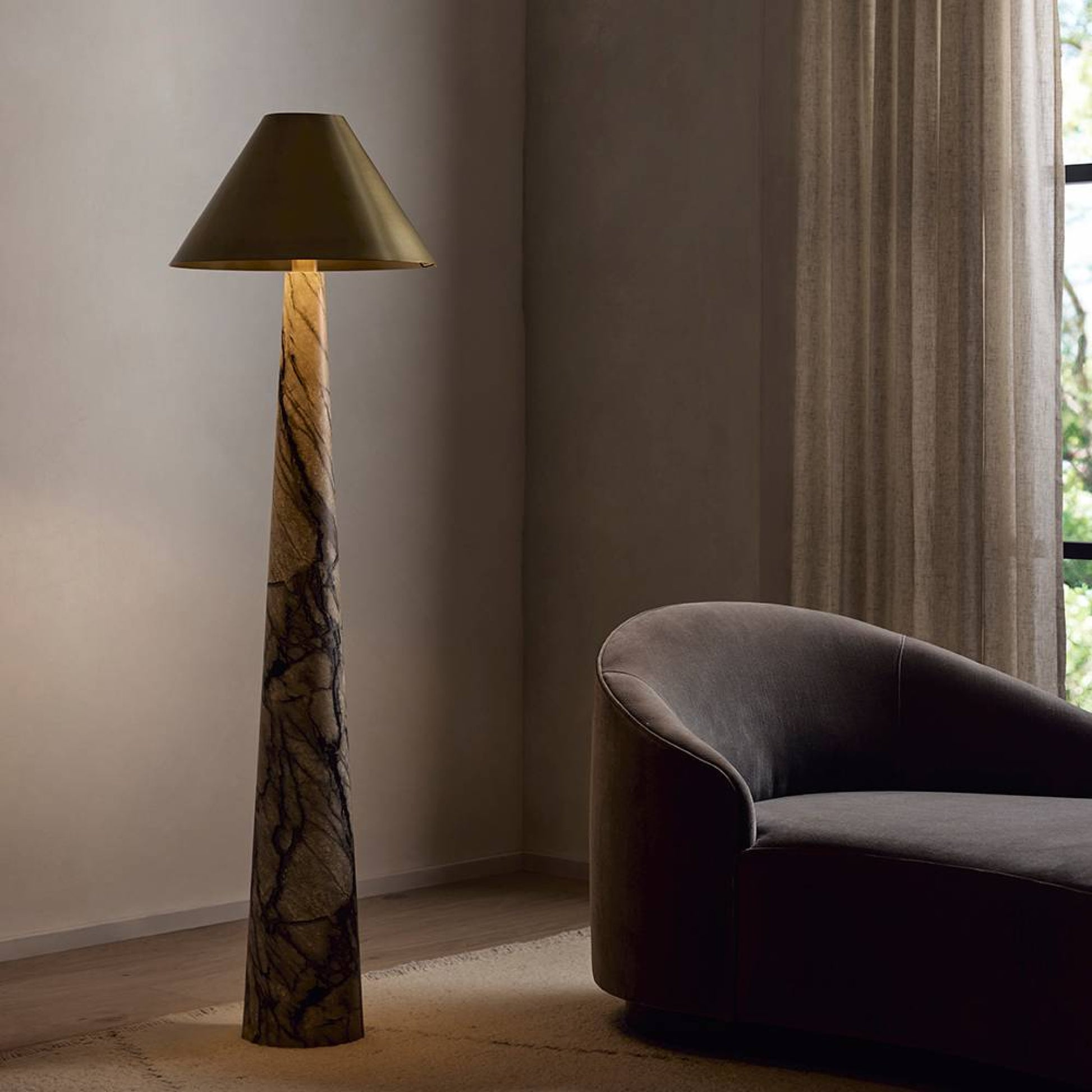 Floor lamp with a textured base and gold shade next to a gray sofa in a room with a window.