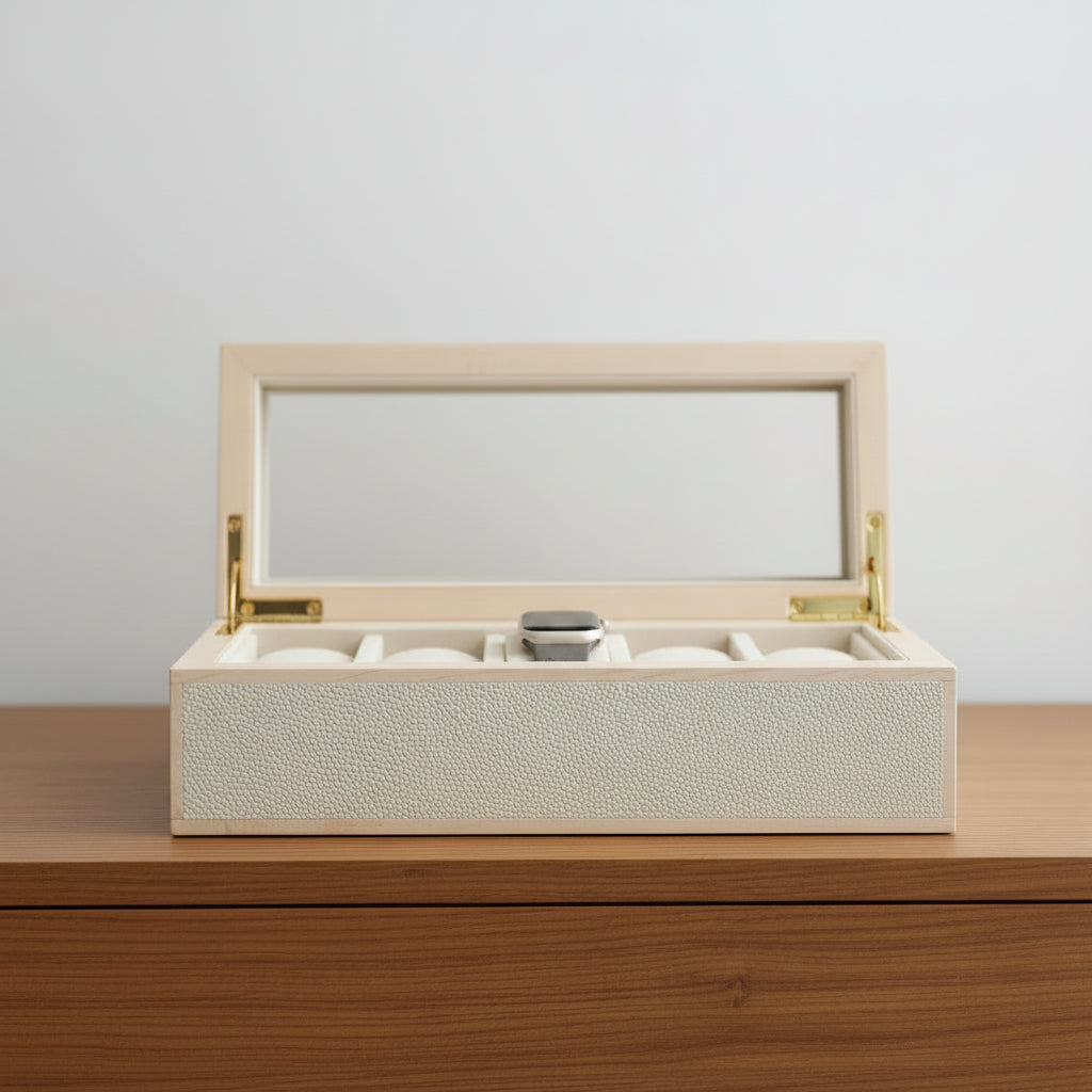 A light natural wood watch box with a clear glass lid, gold-tone hinges, and a cream-colored interior cushion holding five watch slots, shown open on a light gray background.