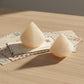 Two pale cream-colored faceted crystal-like ornaments displayed on top of vintage postcards against a clean white background.