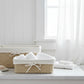 Two woven natural-fiber storage baskets with white fabric liners and bow details, styled with white towels on a clean white background.