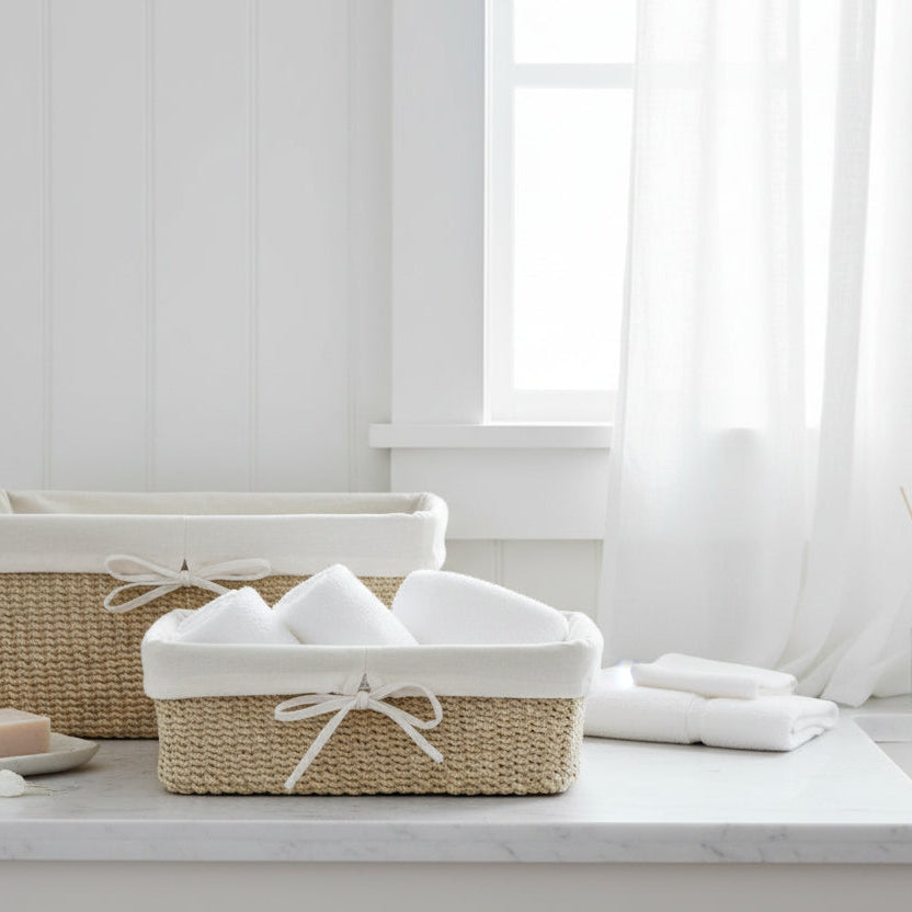 Two woven natural-fiber storage baskets with white fabric liners and bow details, styled with white towels on a clean white background.