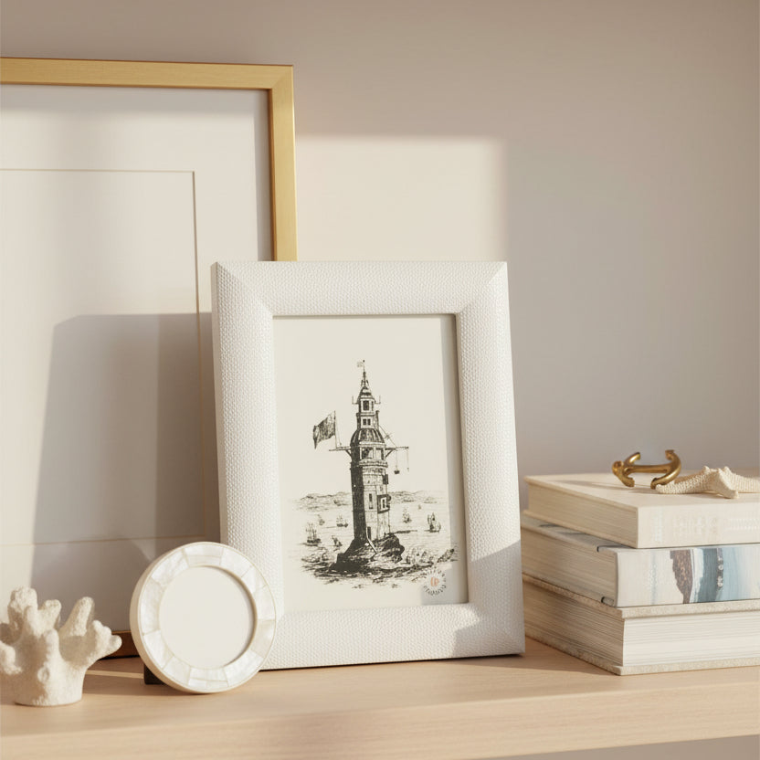 A small white textured picture frame holding a black-and-white illustration of a lighthouse, photographed against a clean white background.