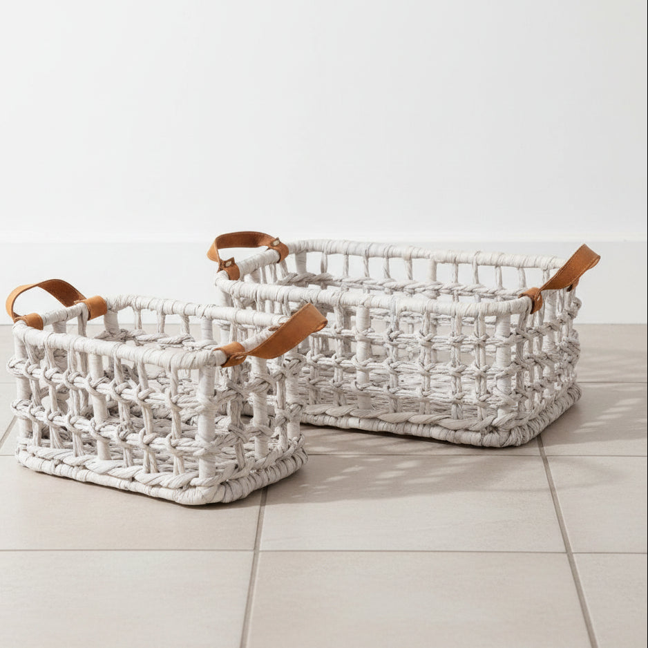 Two woven rectangular storage baskets in a light natural fiber with tan leather handles, photographed on a clean white studio background.