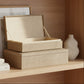 Two stacked rectangular storage boxes with a woven natural fiber texture, shown on a clean white background. The top box has its lid propped open, revealing a light beige interior.