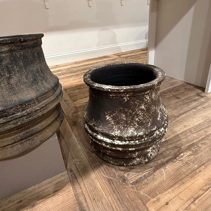 Two large black pots on a wooden floor with a white wall in the background.