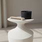 White side table with a black candle and white book on a neutral background