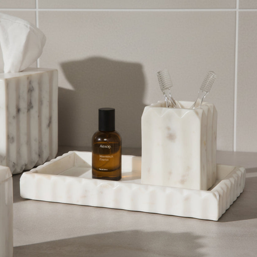 Marble tray with Aesop bottle and toothbrush holder against a tiled wall.