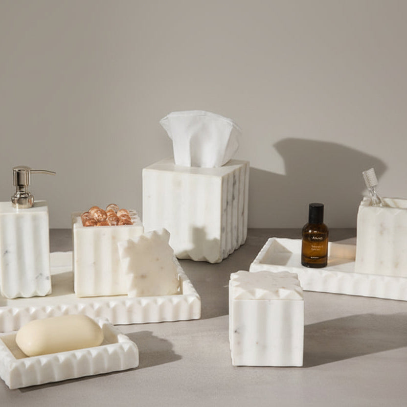 Marble bathroom accessories including a soap dish, tissue holder, and soap on a brown tiled wall background.