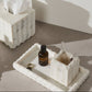 Marble-textured tissue box and tray with skincare products on a neutral background
