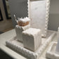 White decorative items including a cube and toothpick holder on a marble surface.