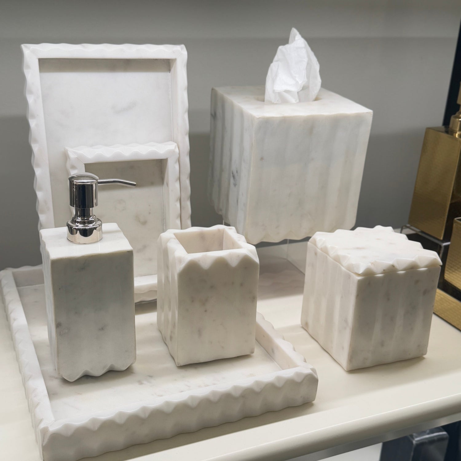 Marble bathroom accessories including a soap dispenser, holder, and decorative pieces on a reflective surface.